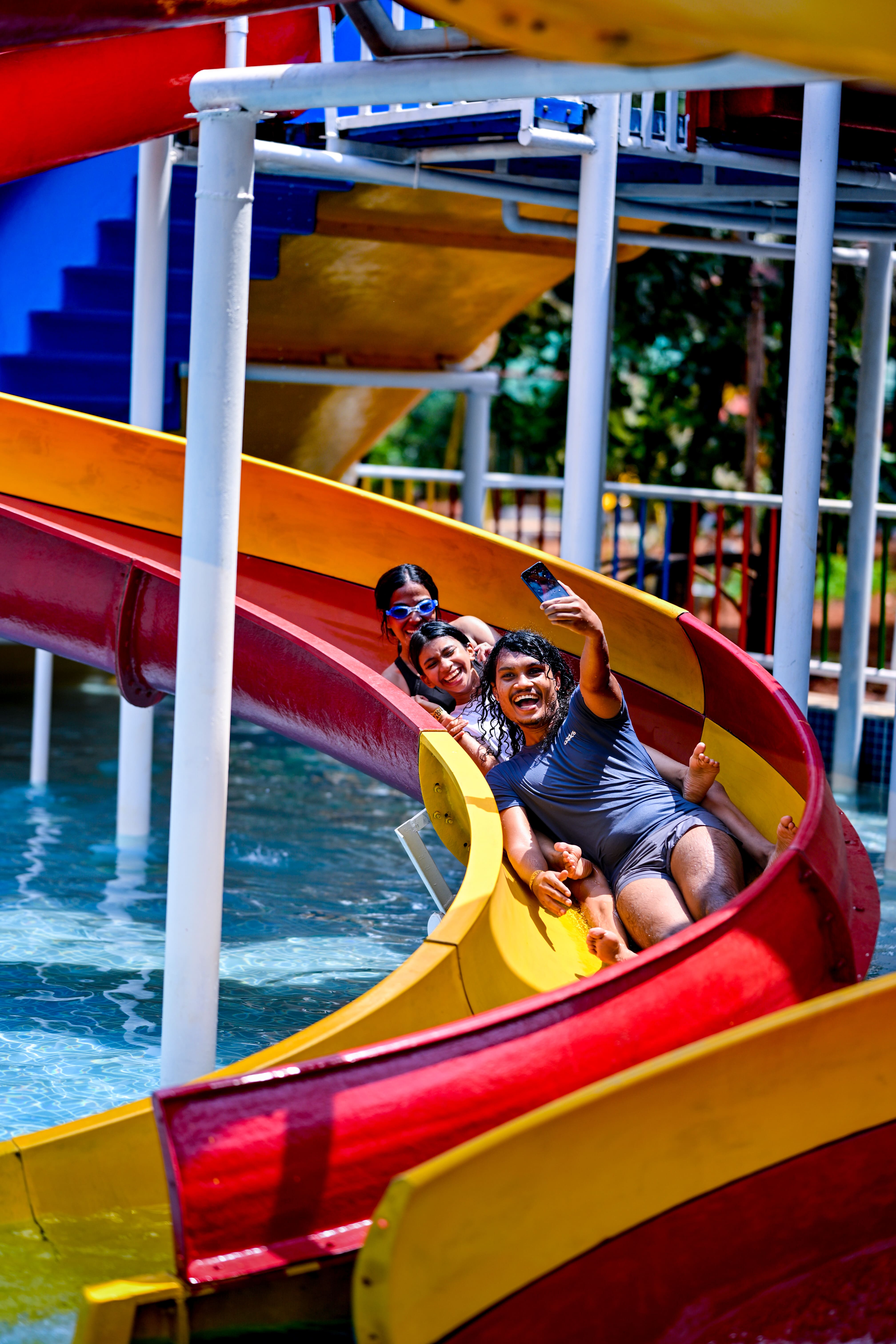 A group of friends enjoying a thrilling ride down a vibrant, multi-colored water slide at Goa Aqua World, capturing their joyful moment with a selfie.